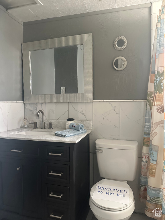 Full bathroom with tile walls, vanity, and toilet