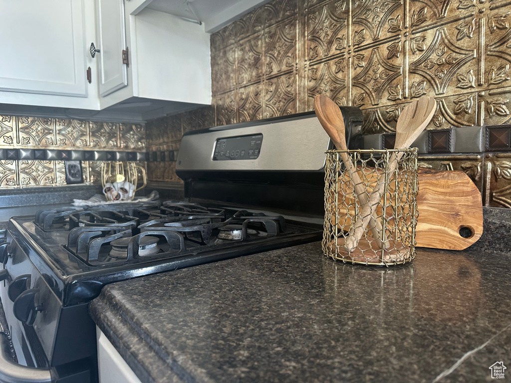Interior details with dark countertops, stainless steel gas range, white cabinetry, and backsplash