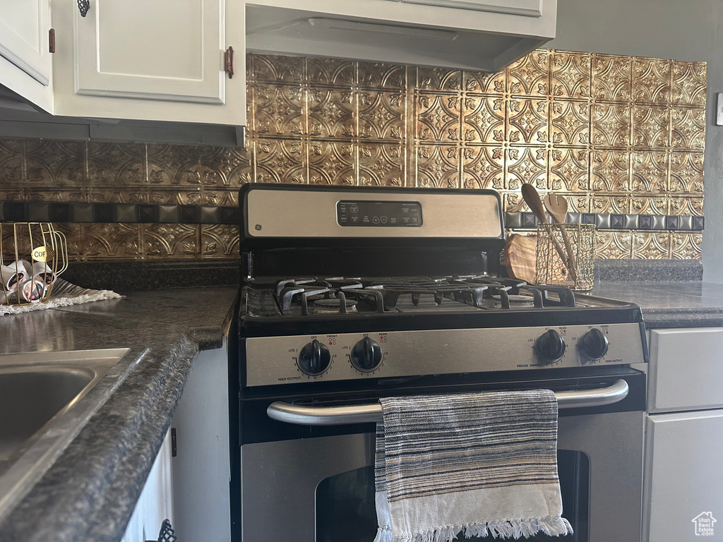 Kitchen featuring decorative backsplash, dark countertops, stainless steel gas range, under cabinet range hood, and white cabinetry
