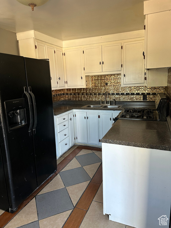 Kitchen featuring white cabinets, sink, backsplash, and black fridge