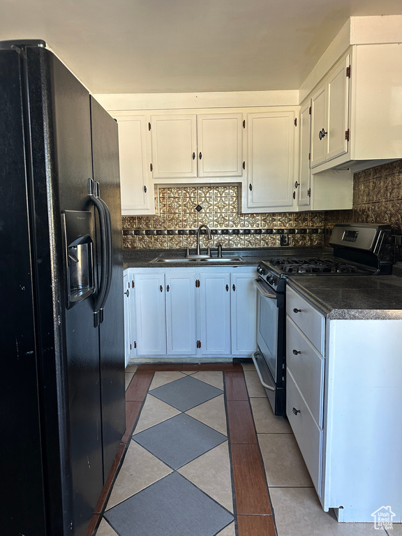 Kitchen featuring black fridge, sink, white cabinets, gas stove, and tasteful backsplash