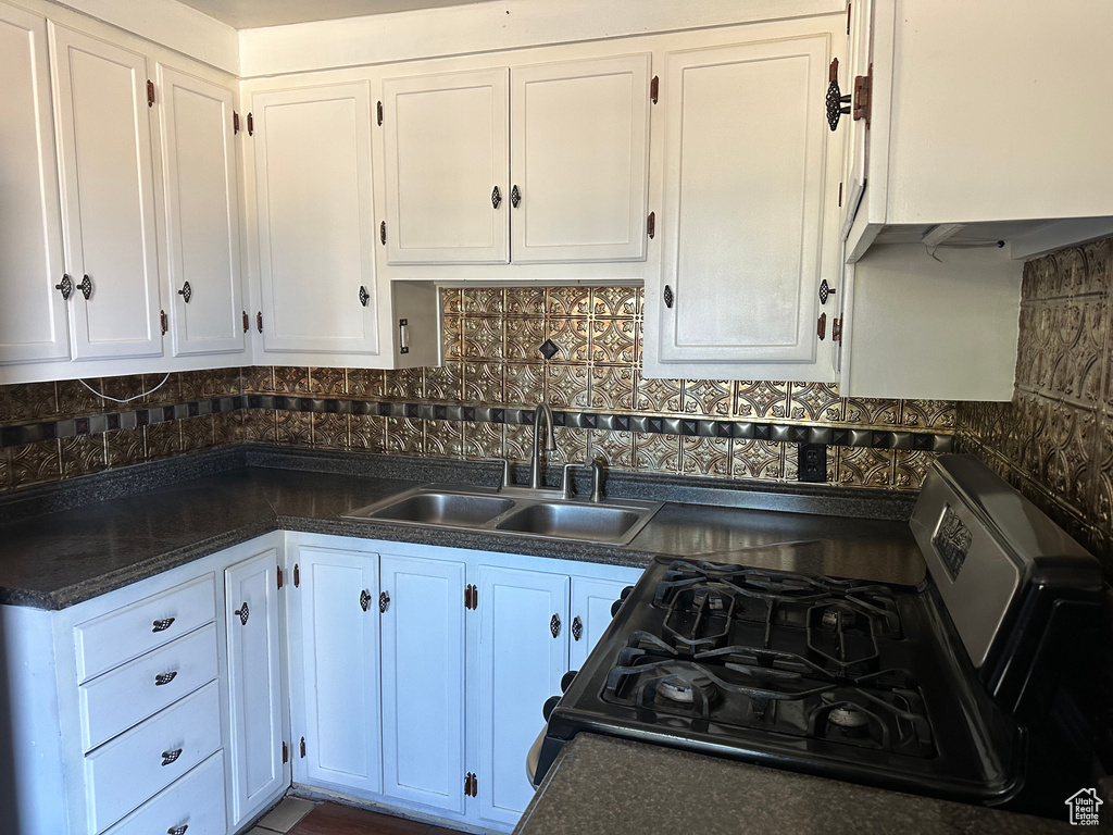 Kitchen featuring black gas range, sink, and white cabinets