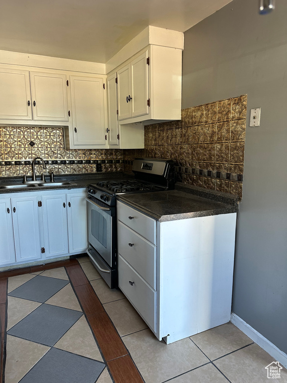Kitchen featuring sink, light tile patterned flooring, white cabinets, gas range, and decorative backsplash