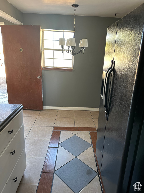 Kitchen with a notable chandelier, decorative light fixtures, black refrigerator with ice dispenser, and light tile patterned floors