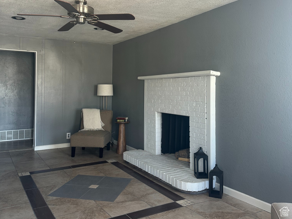 Sitting room featuring ceiling fan, a textured ceiling, a brick fireplace, and baseboards