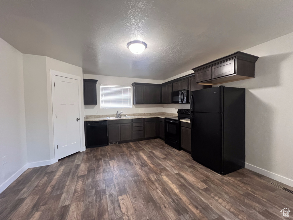 Kitchen with dark brown cabinets, a textured ceiling, dark hardwood / wood-style floors, black appliances, and sink