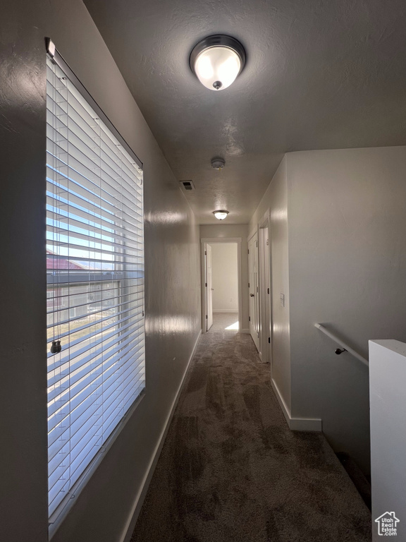 Hall featuring a textured ceiling and dark carpet