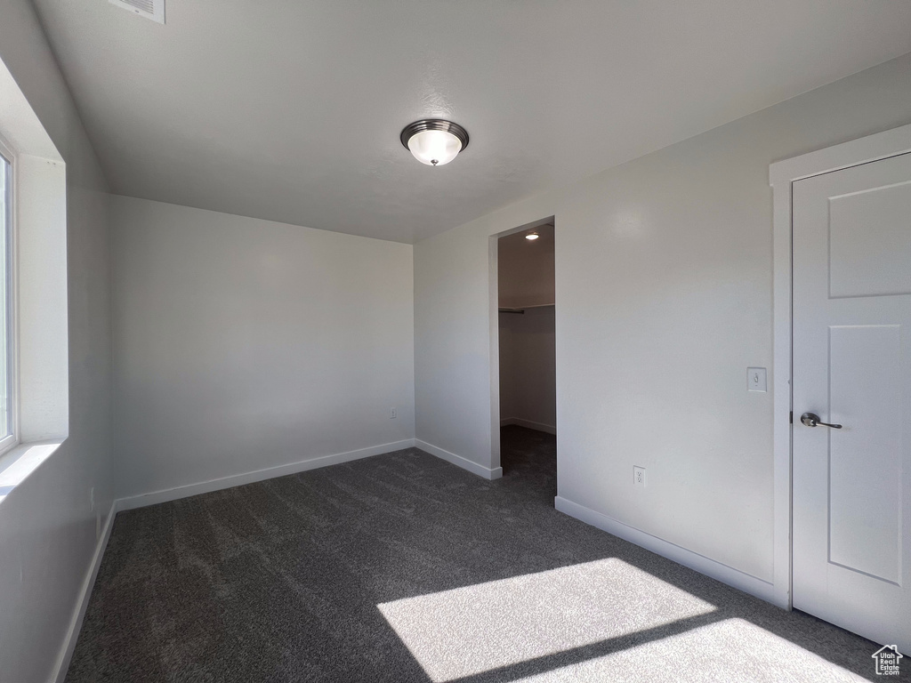 Unfurnished bedroom with a walk in closet, a closet, and dark carpet