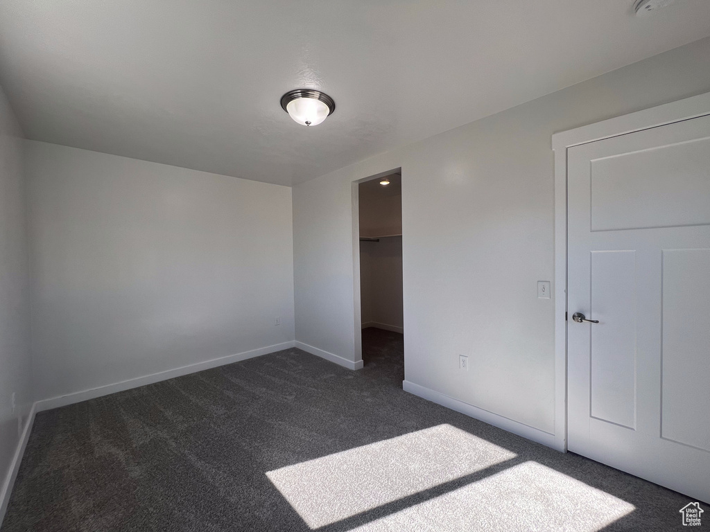 Unfurnished bedroom featuring dark carpet, a walk in closet, and a closet