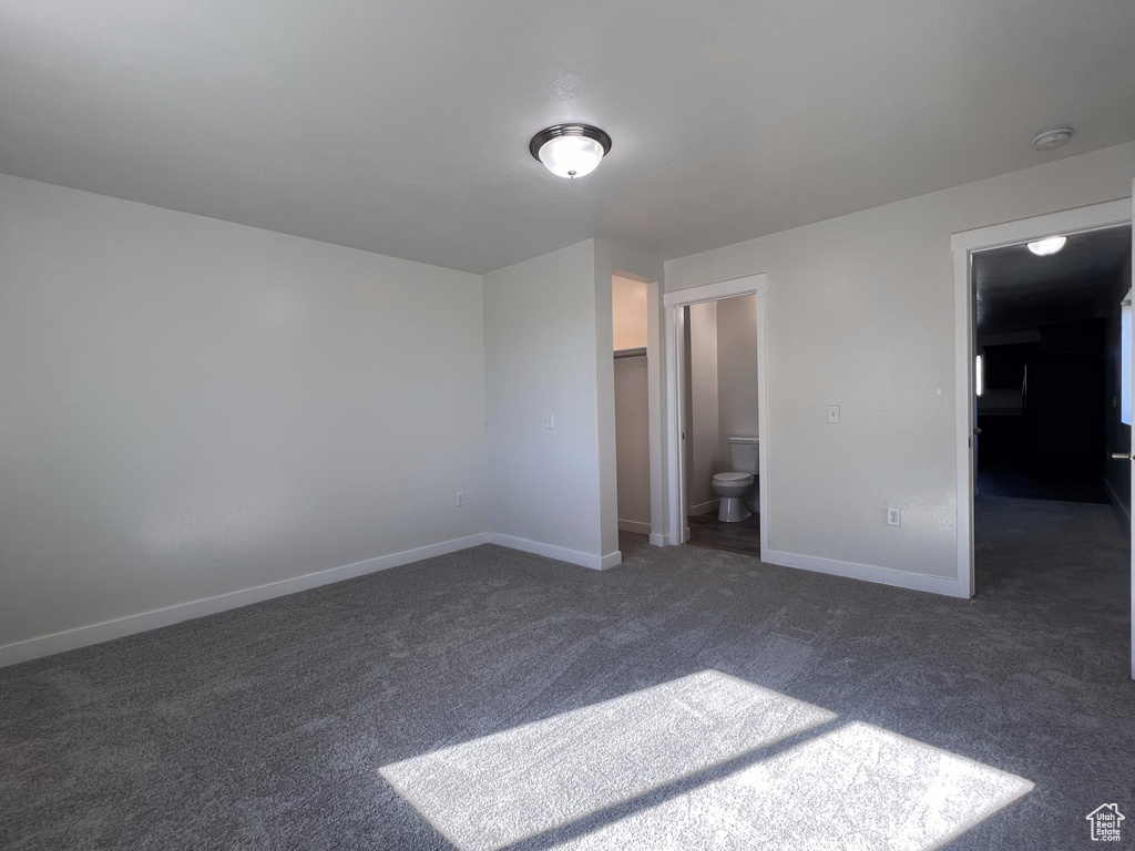 Unfurnished bedroom with a spacious closet, ensuite bathroom, and dark carpet