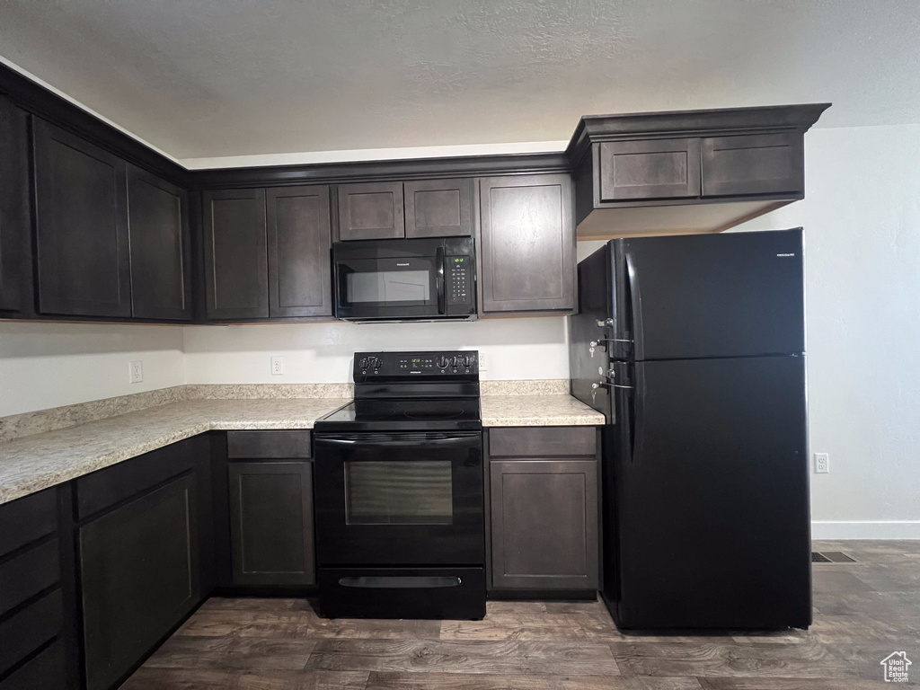 Kitchen with dark brown cabinetry, black appliances, and dark wood-type flooring