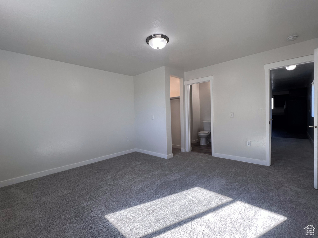 Unfurnished bedroom featuring a spacious closet, connected bathroom, dark carpet, and a closet