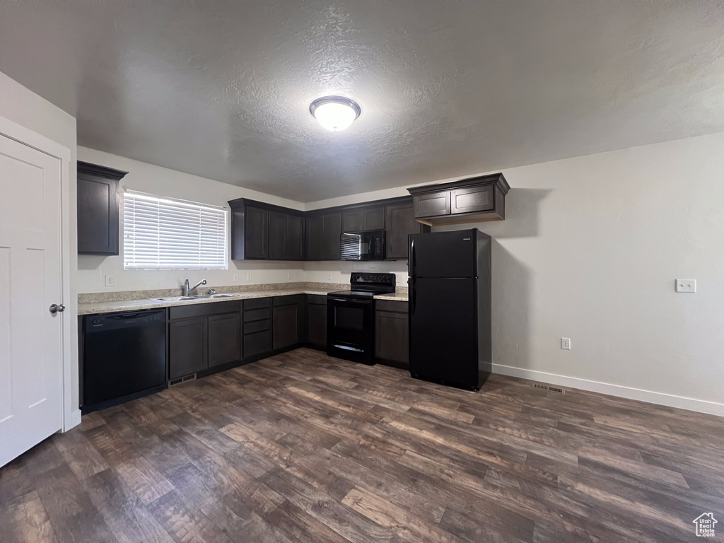 Kitchen featuring dark wood-type flooring, a textured ceiling, black appliances, and sink