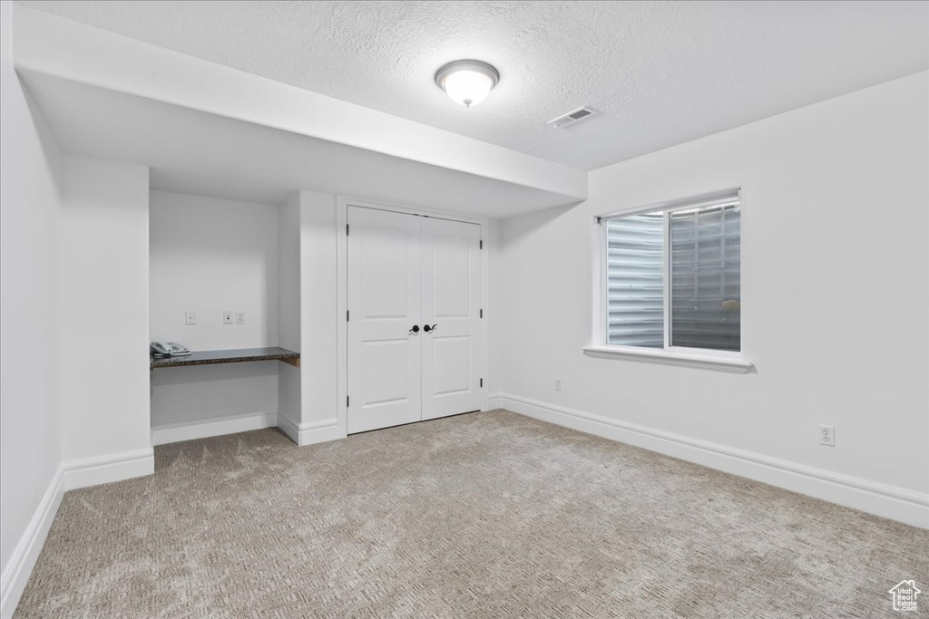 Unfurnished bedroom featuring built in desk, light carpet, a textured ceiling, and a closet