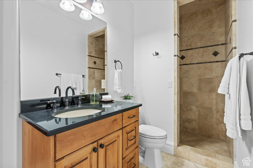 Bathroom featuring vanity, tiled shower, toilet, and tile patterned flooring