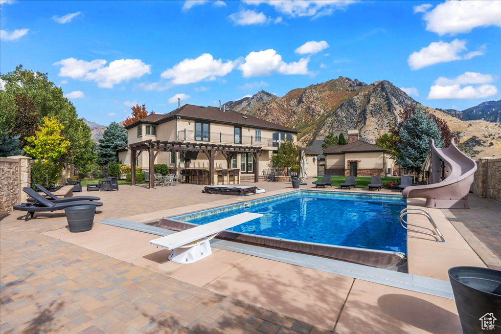 View of pool featuring a patio, a water slide, a mountain view, and a diving board