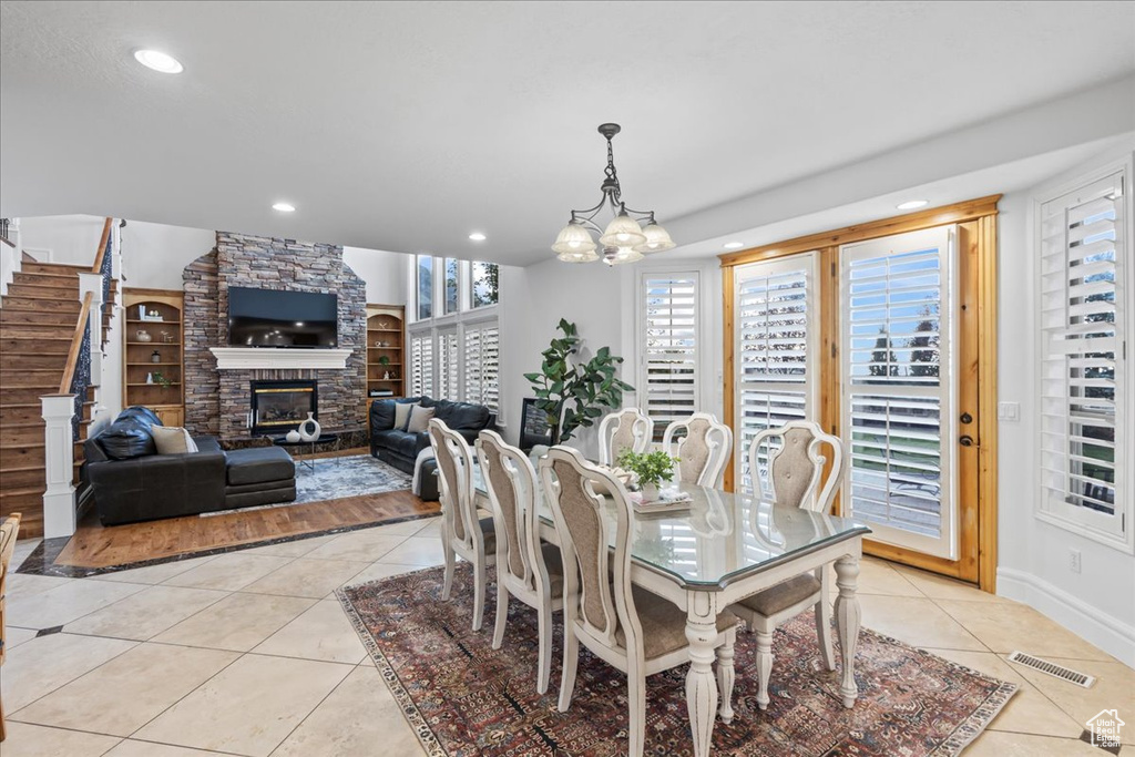 Tiled dining space featuring a stone fireplace and a chandelier