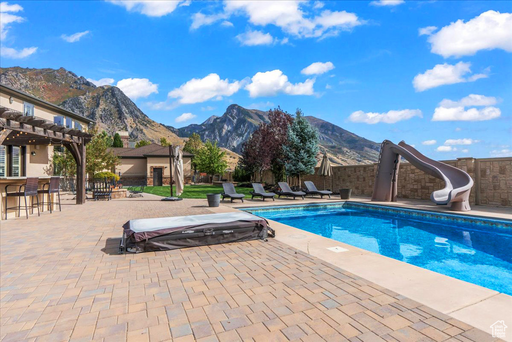 View of swimming pool featuring a pergola, a water slide, a mountain view, and a patio area