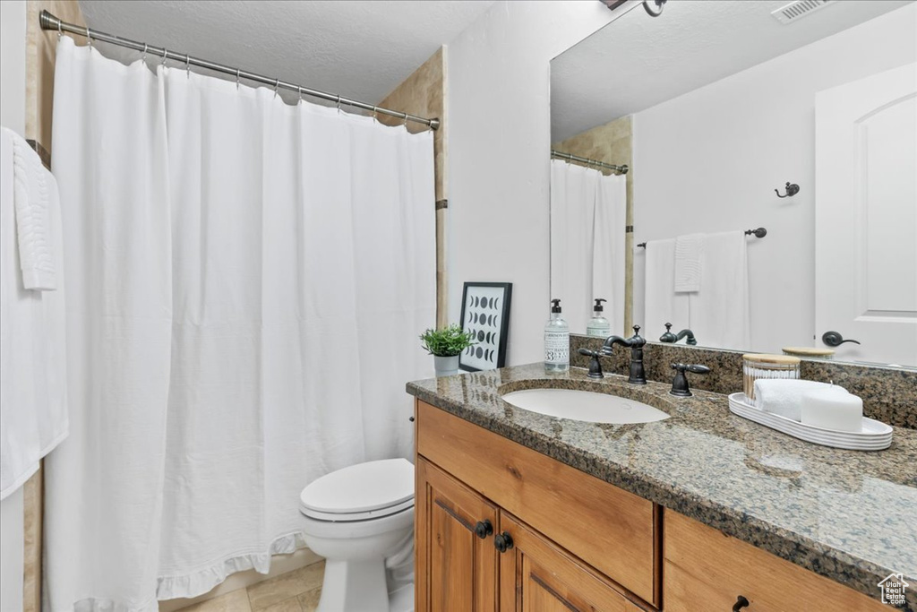 Bathroom featuring toilet, tile patterned flooring, curtained shower, vanity, and a textured ceiling