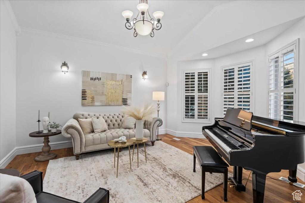 Living room with hardwood / wood-style flooring, ornamental molding, vaulted ceiling, and an inviting chandelier