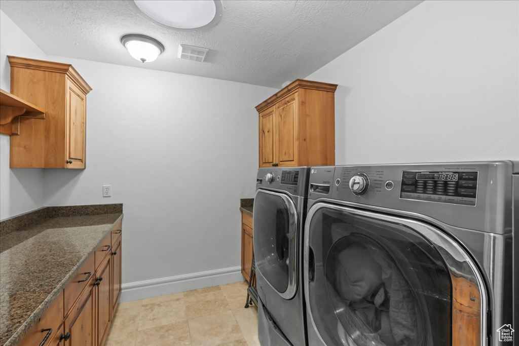 Laundry room featuring a textured ceiling, cabinets, and washer and clothes dryer