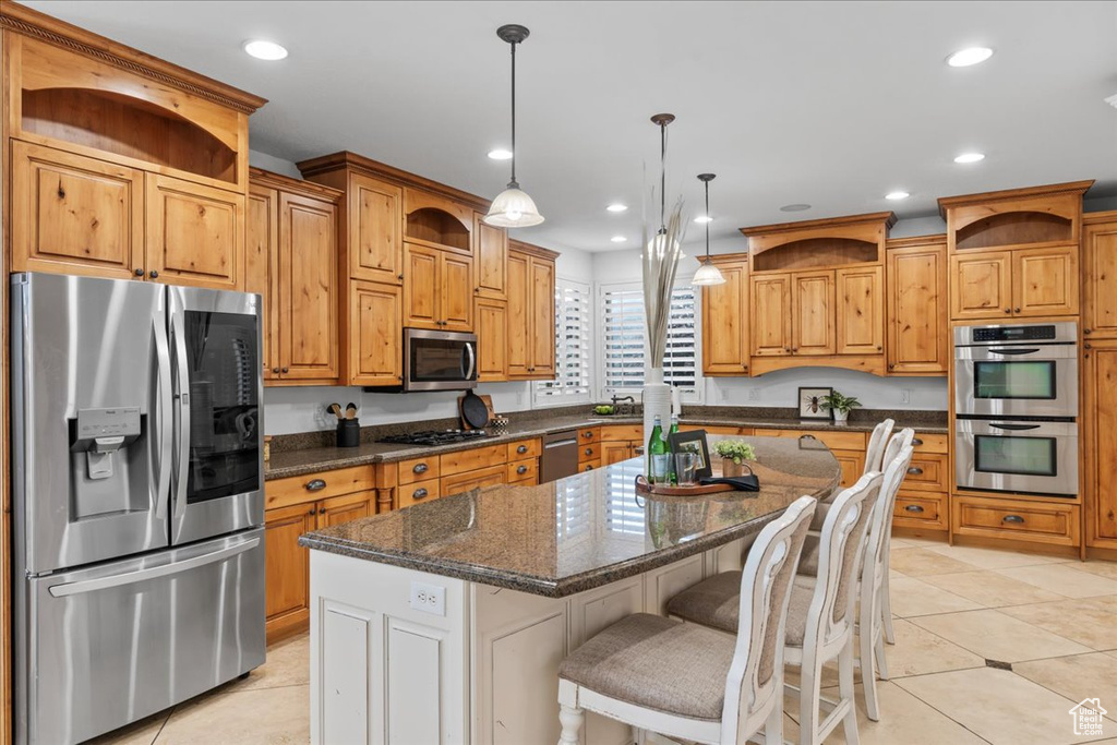 Kitchen with appliances with stainless steel finishes, light tile patterned floors, pendant lighting, and a kitchen island