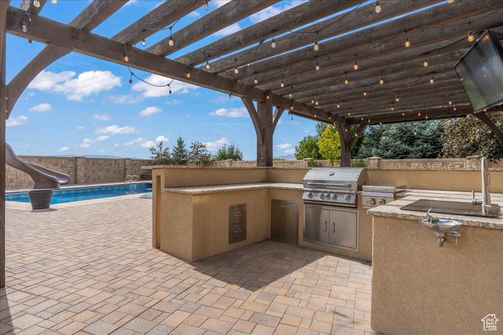 View of patio with a fenced in pool, a pergola, an outdoor kitchen, and grilling area