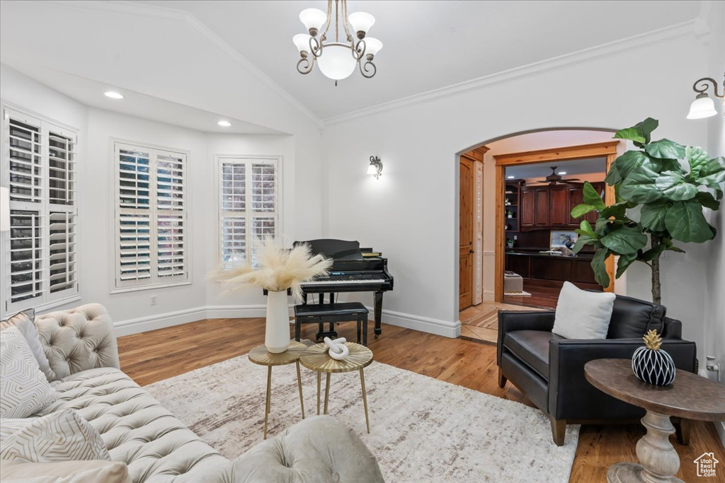 Living room featuring light hardwood / wood-style flooring, ornamental molding, lofted ceiling, and ceiling fan with notable chandelier