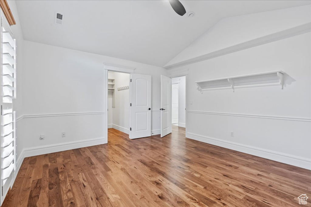 Unfurnished bedroom with a walk in closet, a closet, ceiling fan, lofted ceiling, and hardwood / wood-style flooring