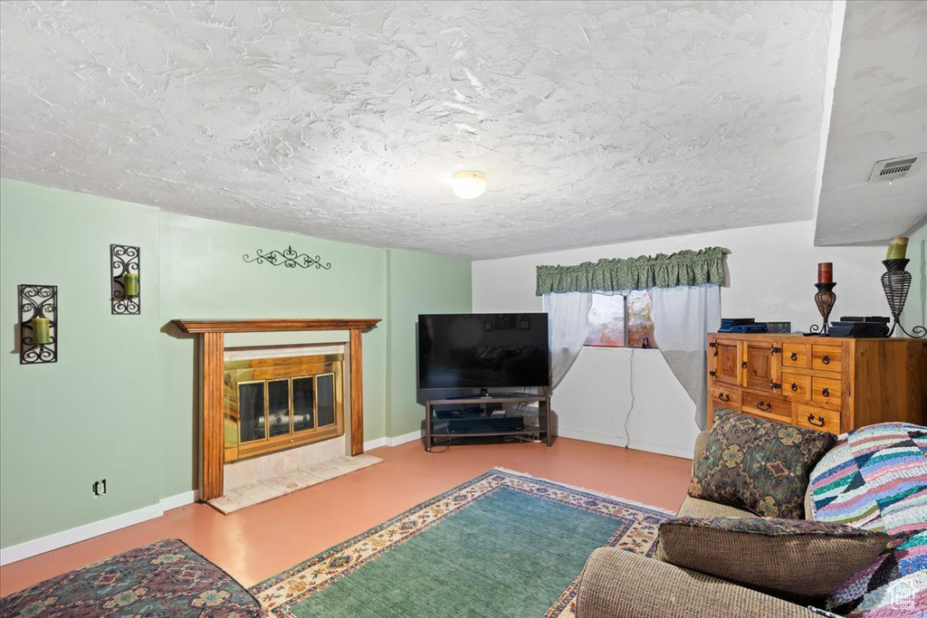 Living room featuring a tiled fireplace, concrete flooring, and a textured ceiling