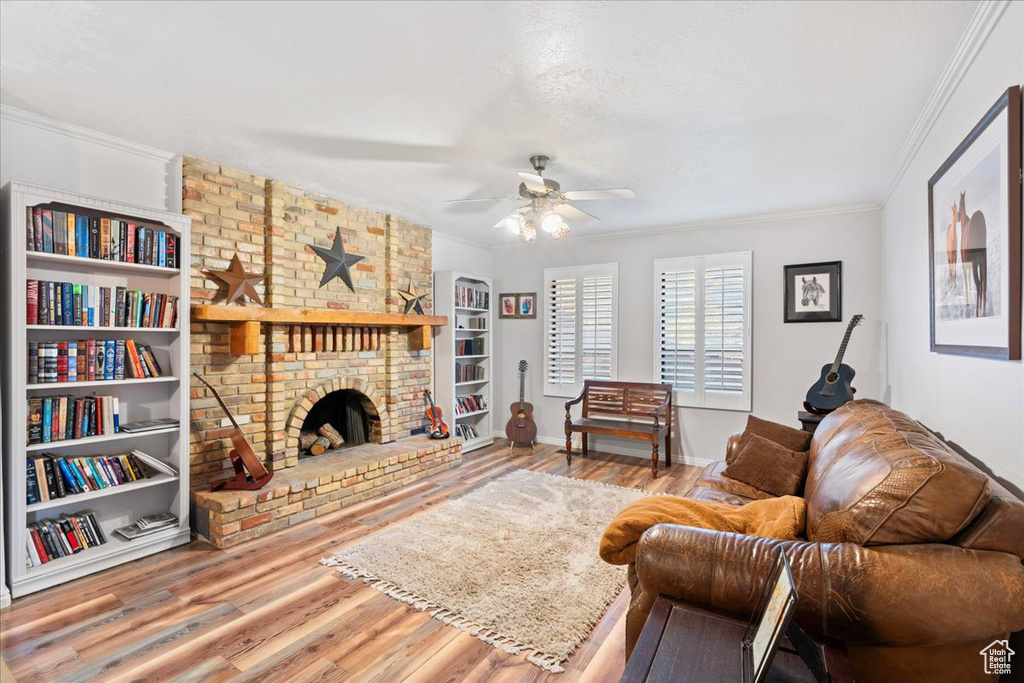 Living room featuring crown molding, hardwood / wood-style flooring, a brick fireplace, and ceiling fan