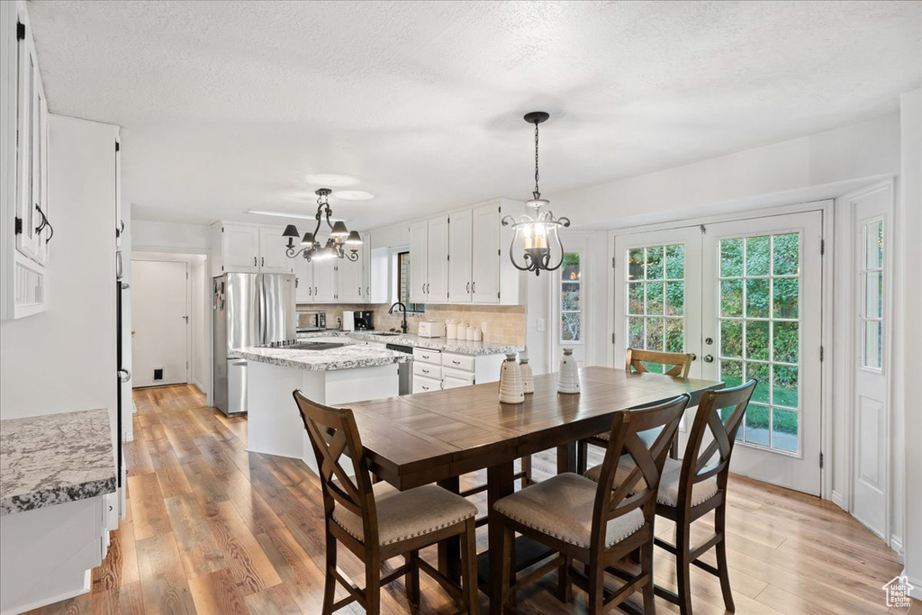 Dining room featuring a textured ceiling, a chandelier, light hardwood / wood-style floors, french doors, and sink