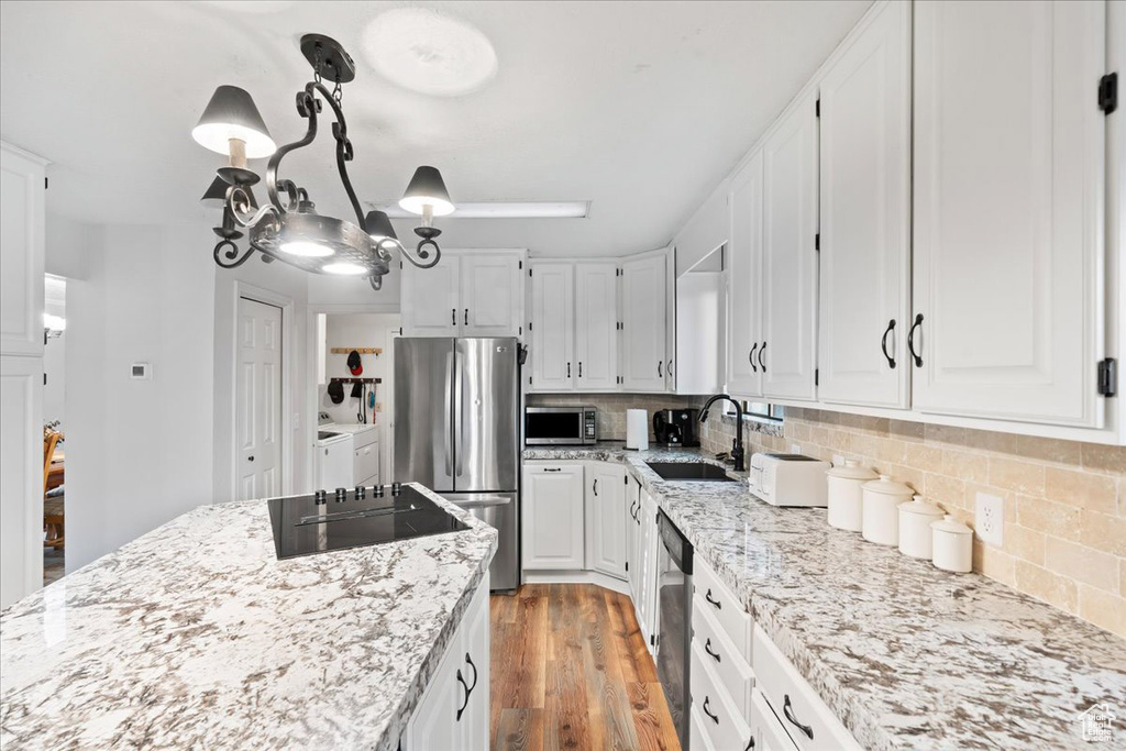 Kitchen featuring appliances with stainless steel finishes, sink, light wood-type flooring, washing machine and clothes dryer, and white cabinetry