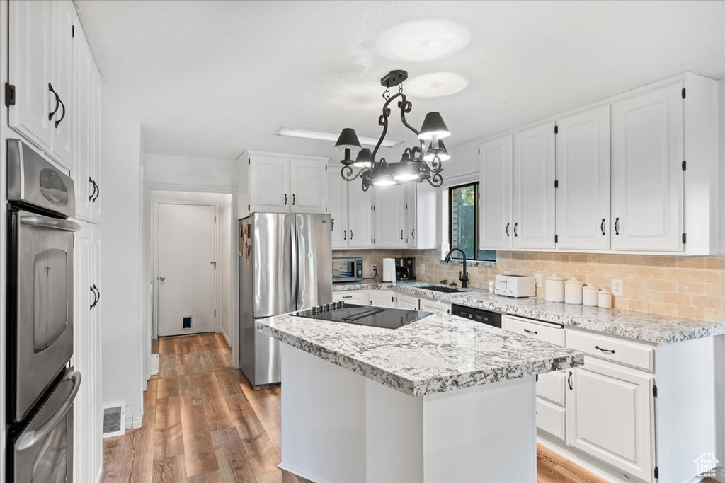 Kitchen with white cabinets, a kitchen island, black appliances, pendant lighting, and light hardwood / wood-style floors