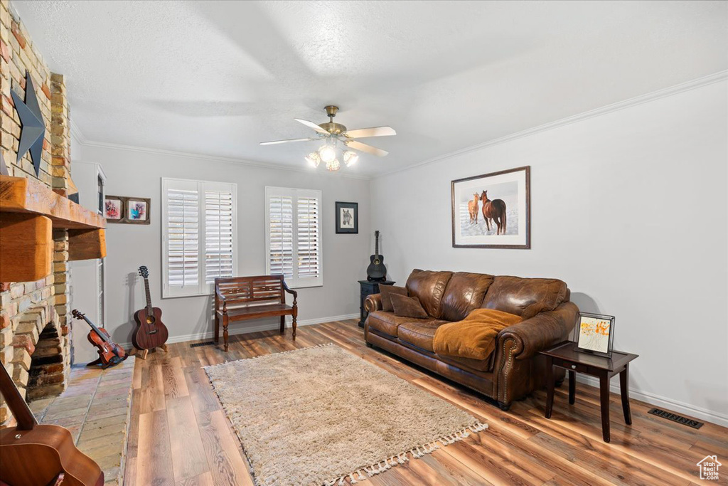 Living room with crown molding, hardwood / wood-style floors, a fireplace, and ceiling fan