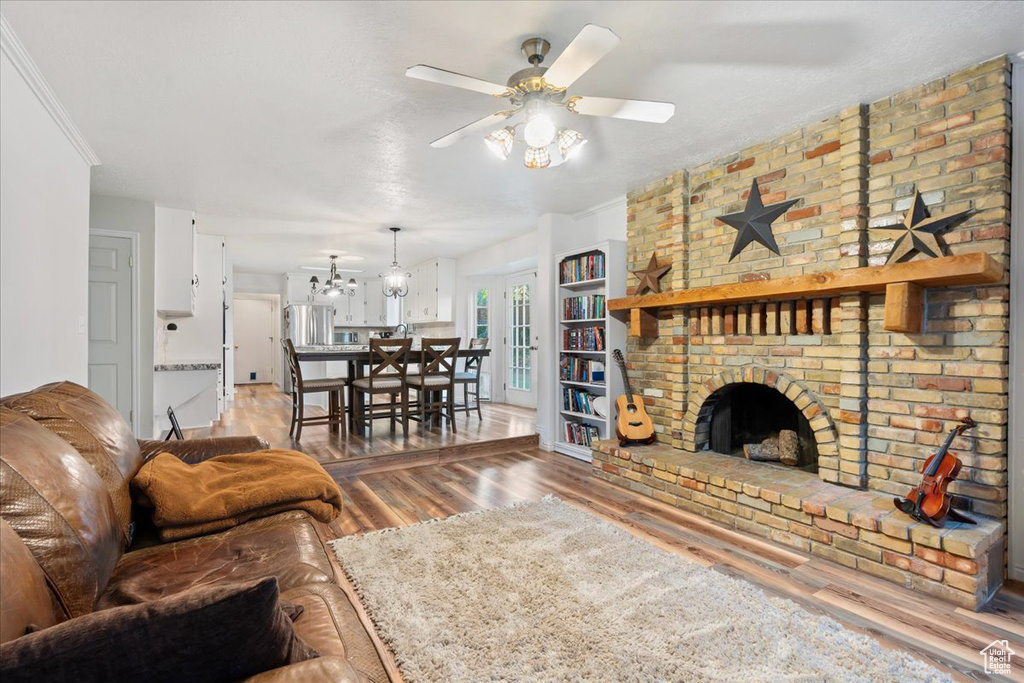 Living room featuring ceiling fan, crown molding, wood-type flooring, and a brick fireplace