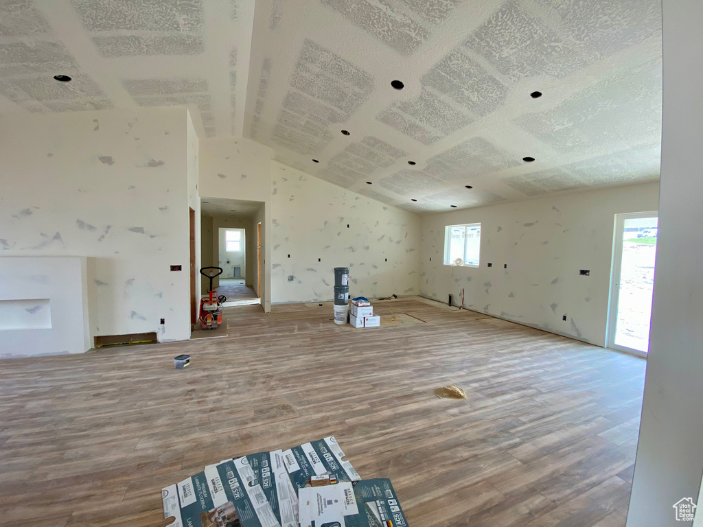 Unfurnished living room with a healthy amount of sunlight, wood-type flooring, and vaulted ceiling