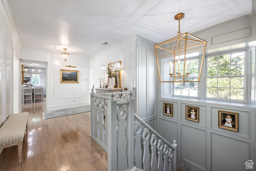 Hall with an inviting chandelier, ornamental molding, and light hardwood / wood-style floors