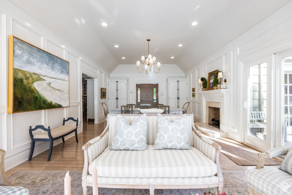 Living room with light hardwood / wood-style floors, lofted ceiling, ornamental molding, and an inviting chandelier