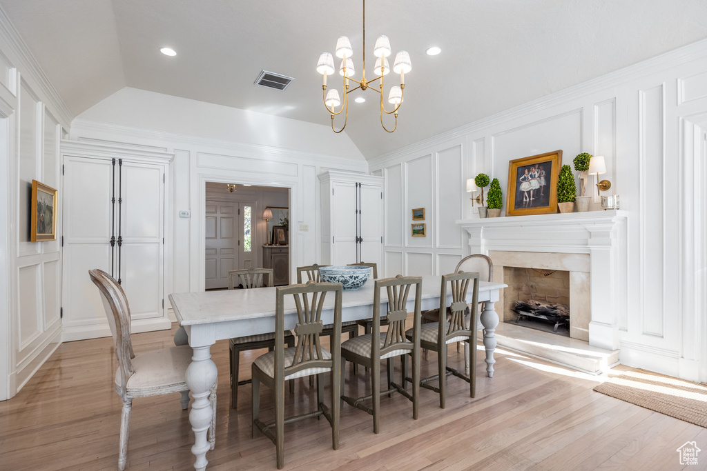 Dining room featuring lofted ceiling, light hardwood / wood-style flooring, ornamental molding, a notable chandelier, and a fireplace