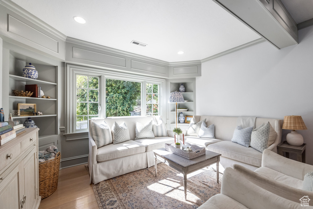 Living room featuring light hardwood / wood-style floors, crown molding, and built in shelves