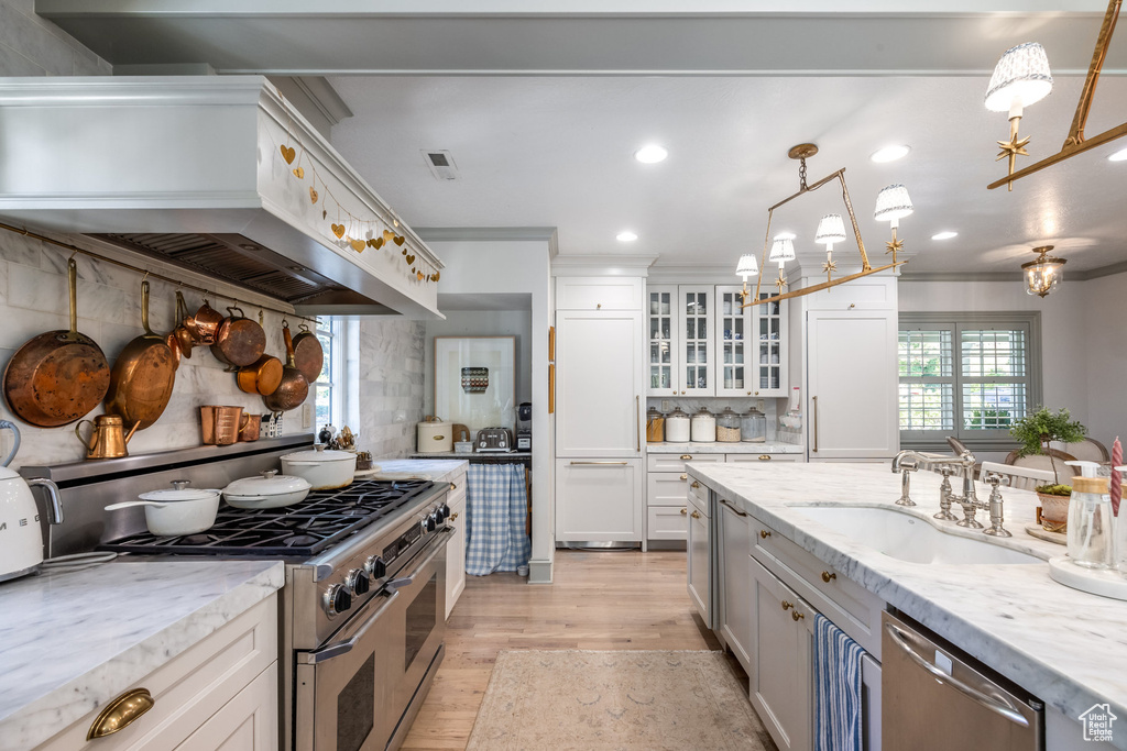 Kitchen featuring white cabinets, hanging light fixtures, light stone counters, sink, and stainless steel appliances