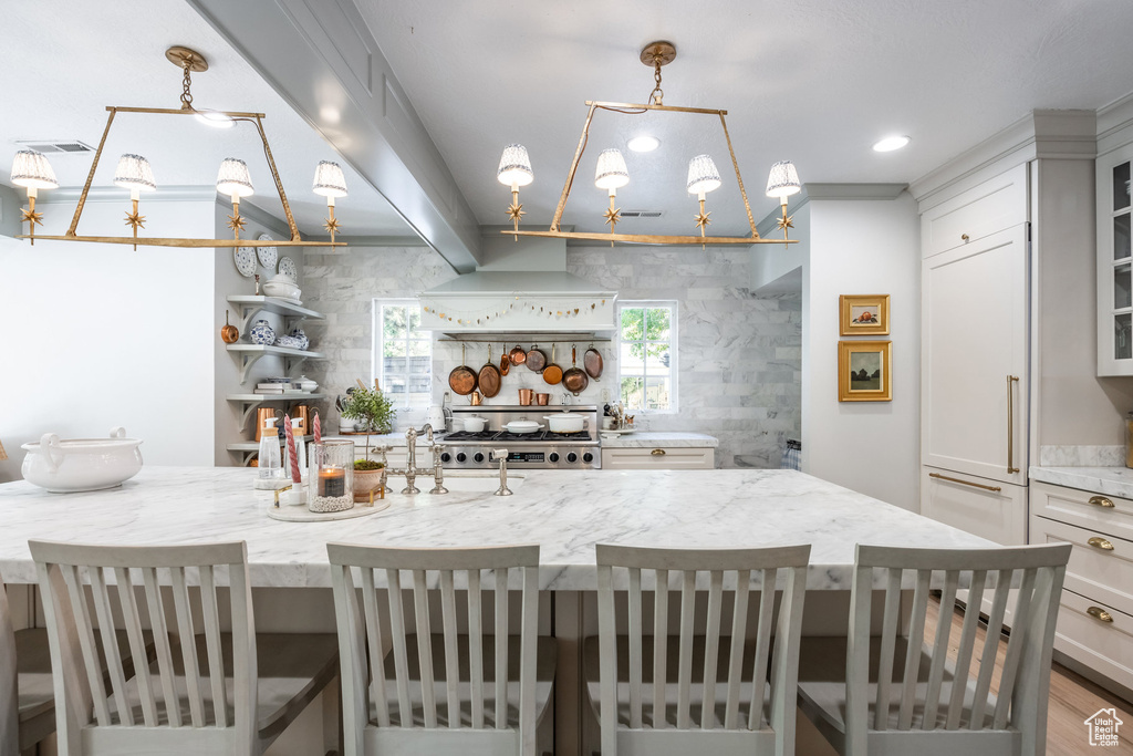 Kitchen with beamed ceiling, a breakfast bar, pendant lighting, custom exhaust hood, and light hardwood / wood-style floors