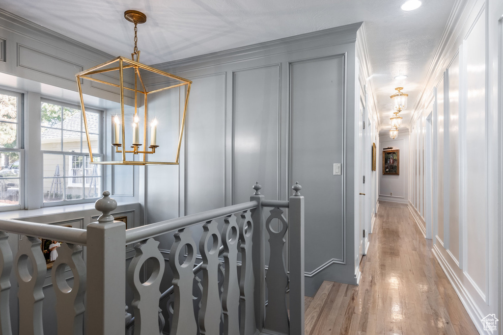 Hallway with a notable chandelier, ornamental molding, and light hardwood / wood-style flooring