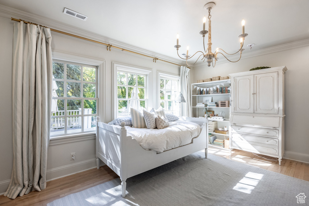 Bedroom with multiple windows, a notable chandelier, light wood-type flooring, and crown molding