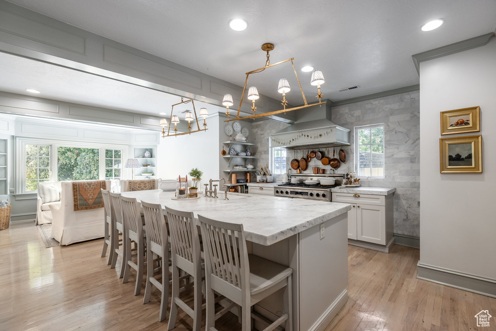 Kitchen with stainless steel range oven, light hardwood / wood-style floors, pendant lighting, custom exhaust hood, and white cabinets