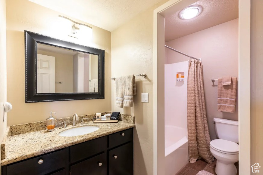 Full bathroom with vanity, a textured ceiling, shower / bath combo with shower curtain, and toilet