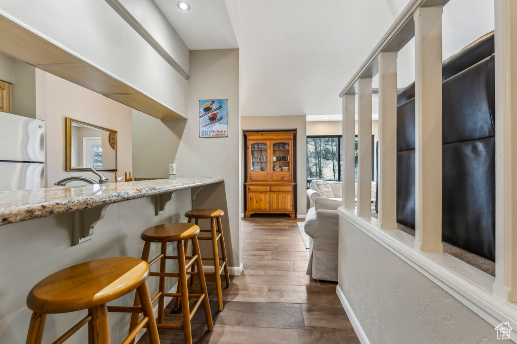 Kitchen featuring dark wood-type flooring, a breakfast bar, a sink, freestanding refrigerator, and light stone countertops