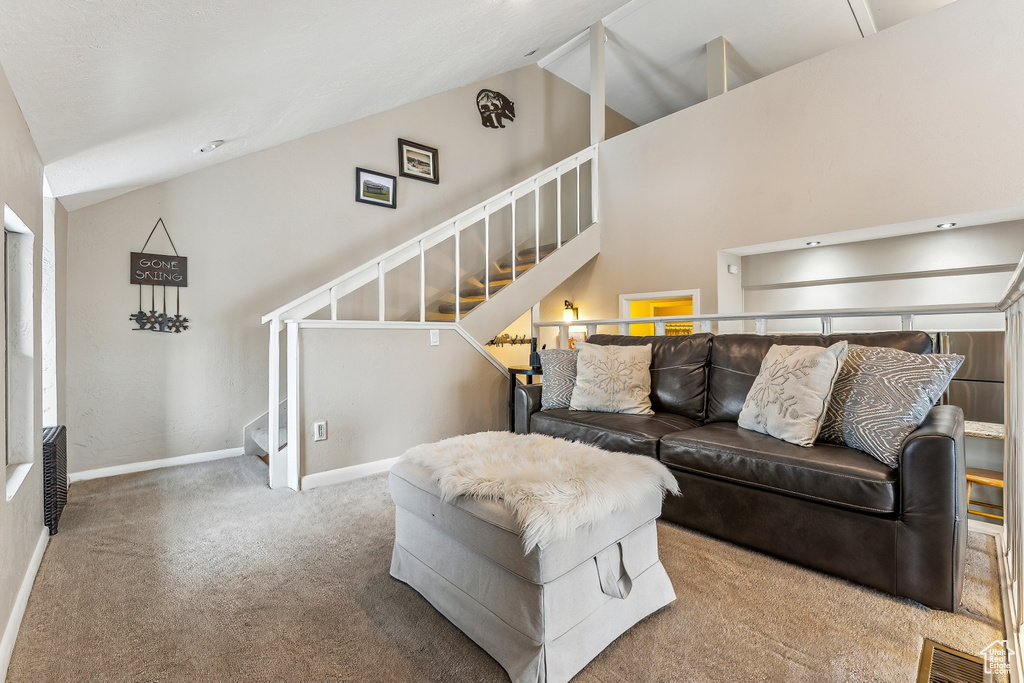 Carpeted living room featuring stairway, baseboards, high vaulted ceiling, and visible vents