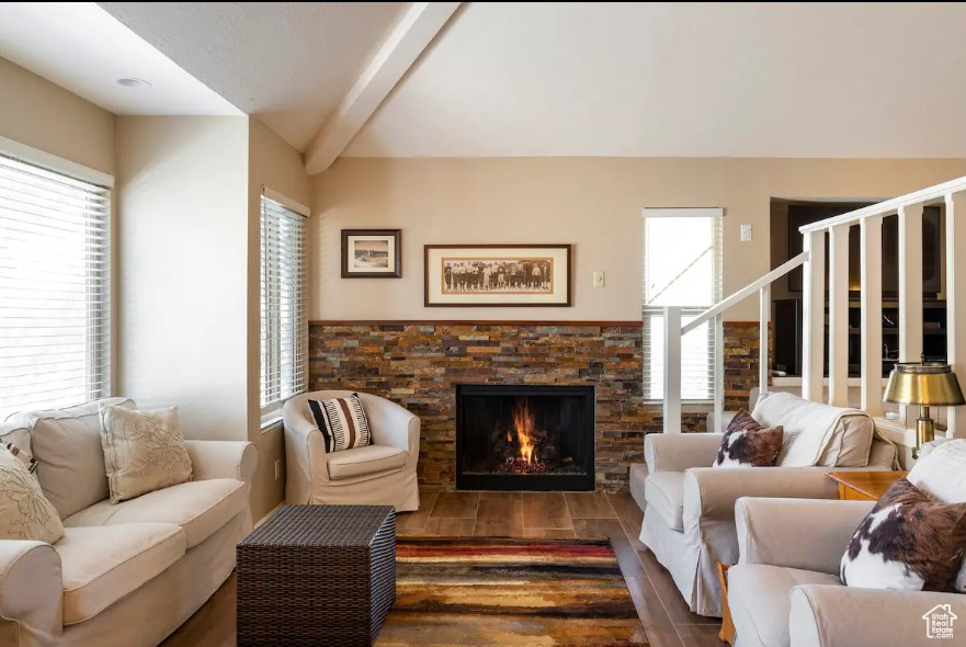 Living room featuring a stone fireplace, dark hardwood / wood-style floors, and beam ceiling